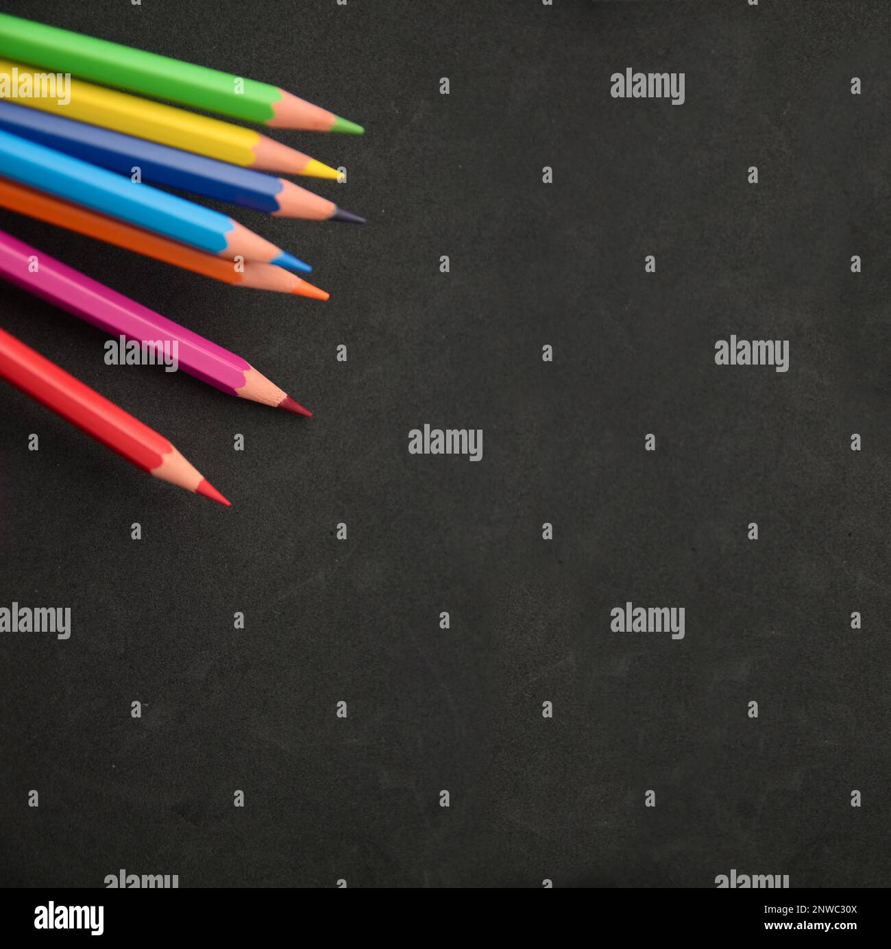 Image de certains crayons de couleur arc-en-ciel sur une surface noire avec un peu de texture et d'espace de copie Banque D'Images