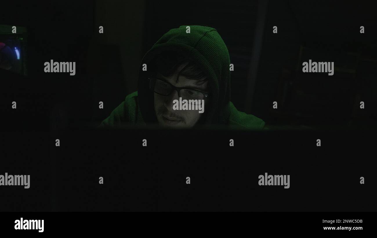 The mystérieux World of Hacking, Young Programmer in Hoodie et Black Glass immergés dans Coding with Green Illumination Banque D'Images