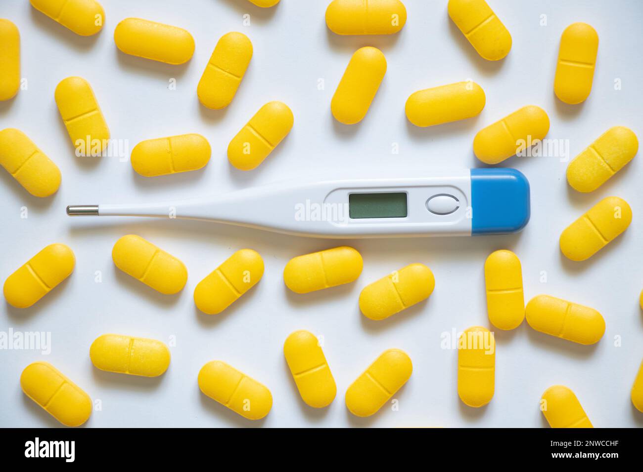 le thermomètre électronique se trouve à côté des pilules jaunes sur un fond isolé, la médecine et la pharmacie, la santé et le traitement, les pilules et les antibiotiques Banque D'Images