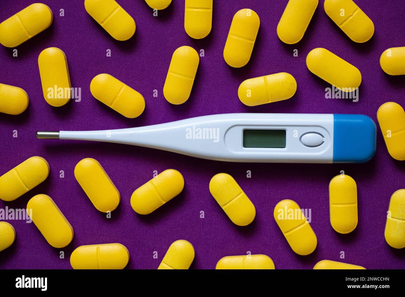 le thermomètre électronique se trouve à côté des pilules jaunes sur un fond isolé, la médecine et la pharmacie, la santé et le traitement, les pilules et les antibiotiques Banque D'Images