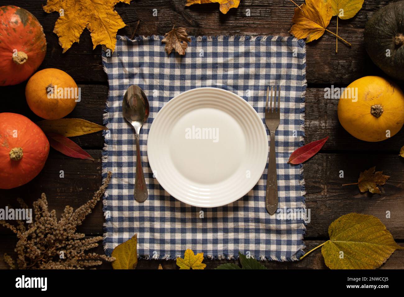 plaque blanche sur la nappe se dresse sur une table en bois à côté des citrouilles et des feuilles d'automne, table d'automne festive, plats sur la table Banque D'Images