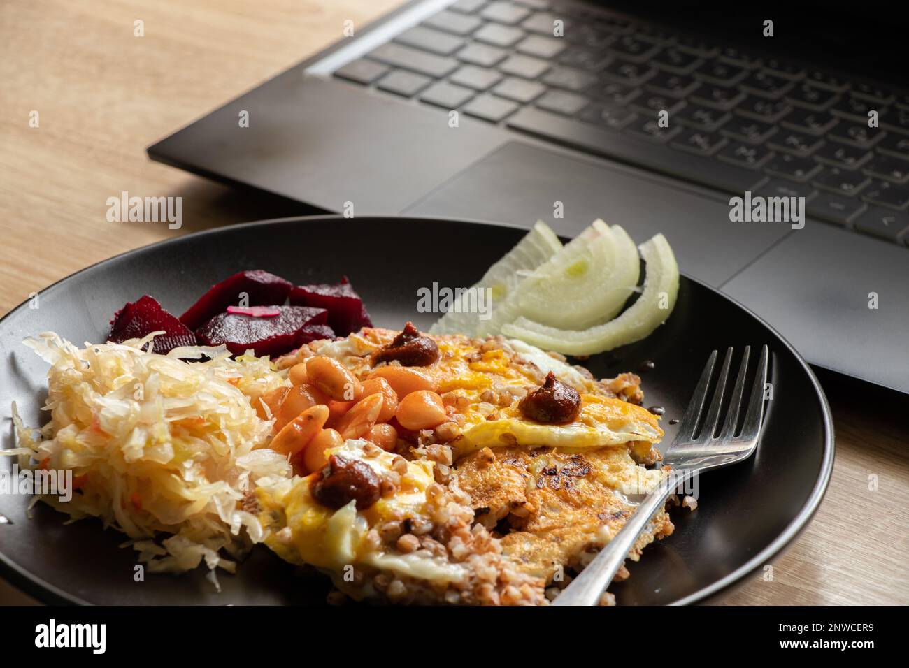 œufs brouillés avec des légumes dans une assiette noire près d'un ordinateur portable à une table sur un robta, déjeuner sur le lieu de travail, une assiette de nourriture sur le lieu de travail Banque D'Images