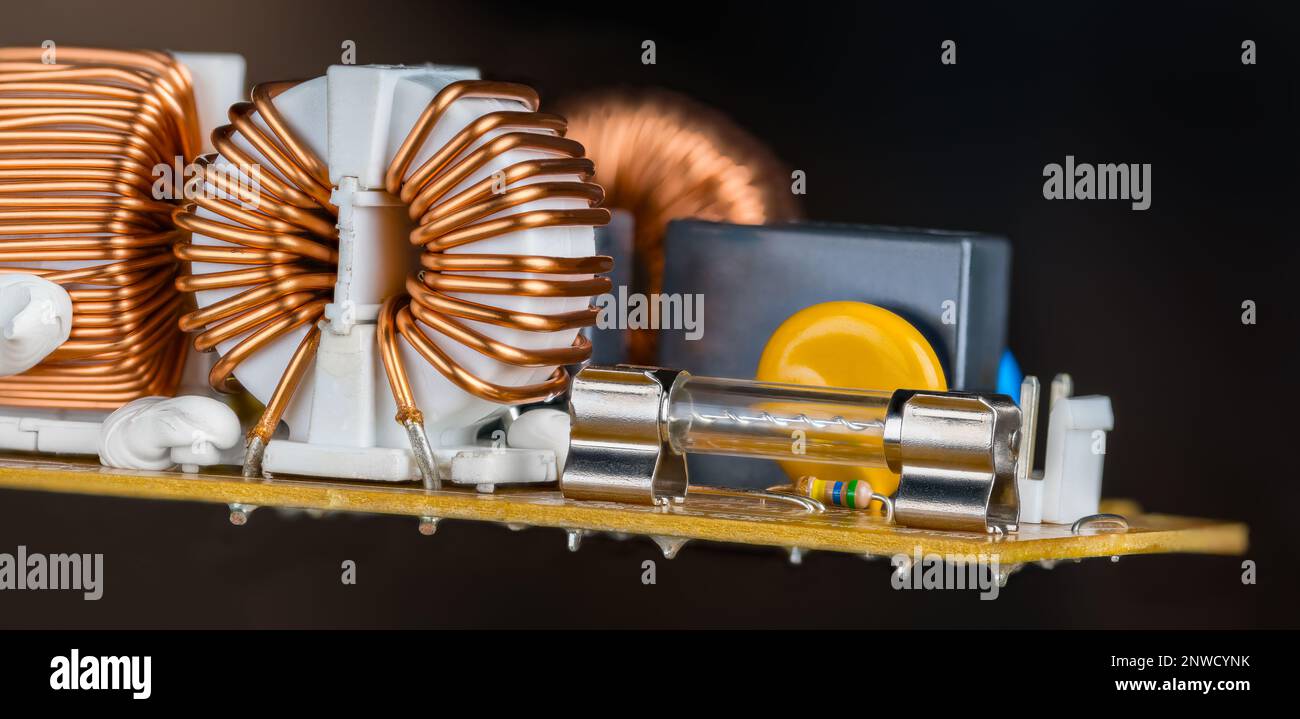 Fusible électrique en verre ou bobine toroïde fil de cuivre dans la carte de circuit imprimé stationnaire sur fond noir. Inductances recouvertes de plastique blanc fixé par pâte de silicone. Banque D'Images