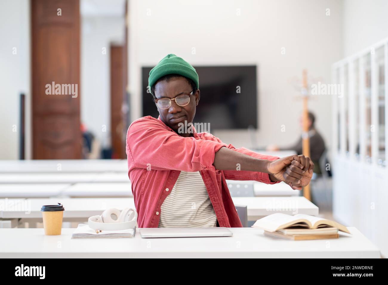 Un étudiant africain fatigué, qui étire les mains, détend l'esprit et les muscles après une étude intense en bibliothèque Banque D'Images