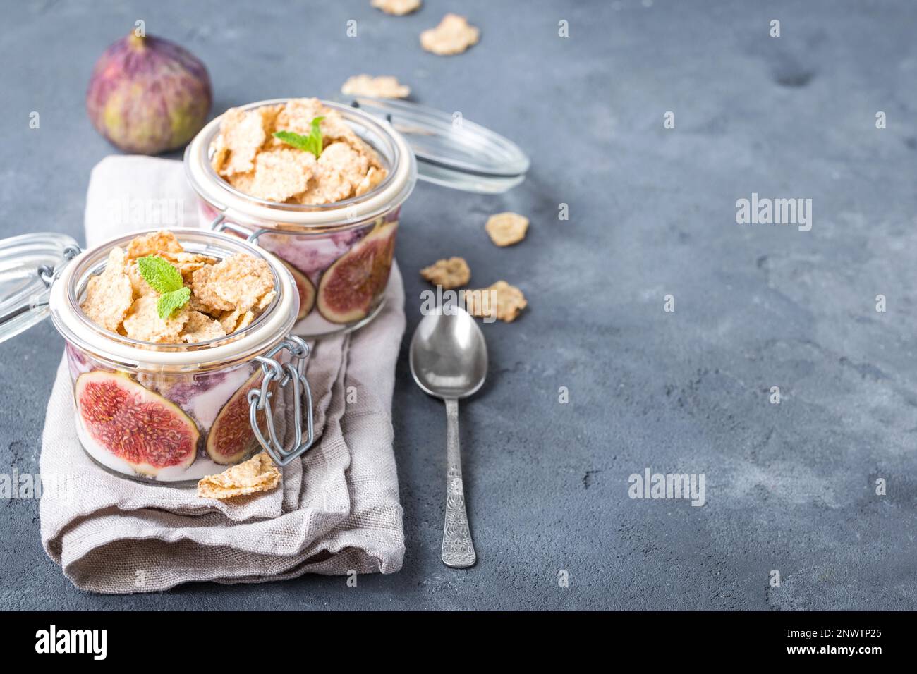 Yaourt santé fait maison dans une casserole en verre avec céréales, figues, menthe sur fond de pierre rustique. Espace pour le texte. Petit déjeuner sain le matin. Fraîchement préparé Banque D'Images