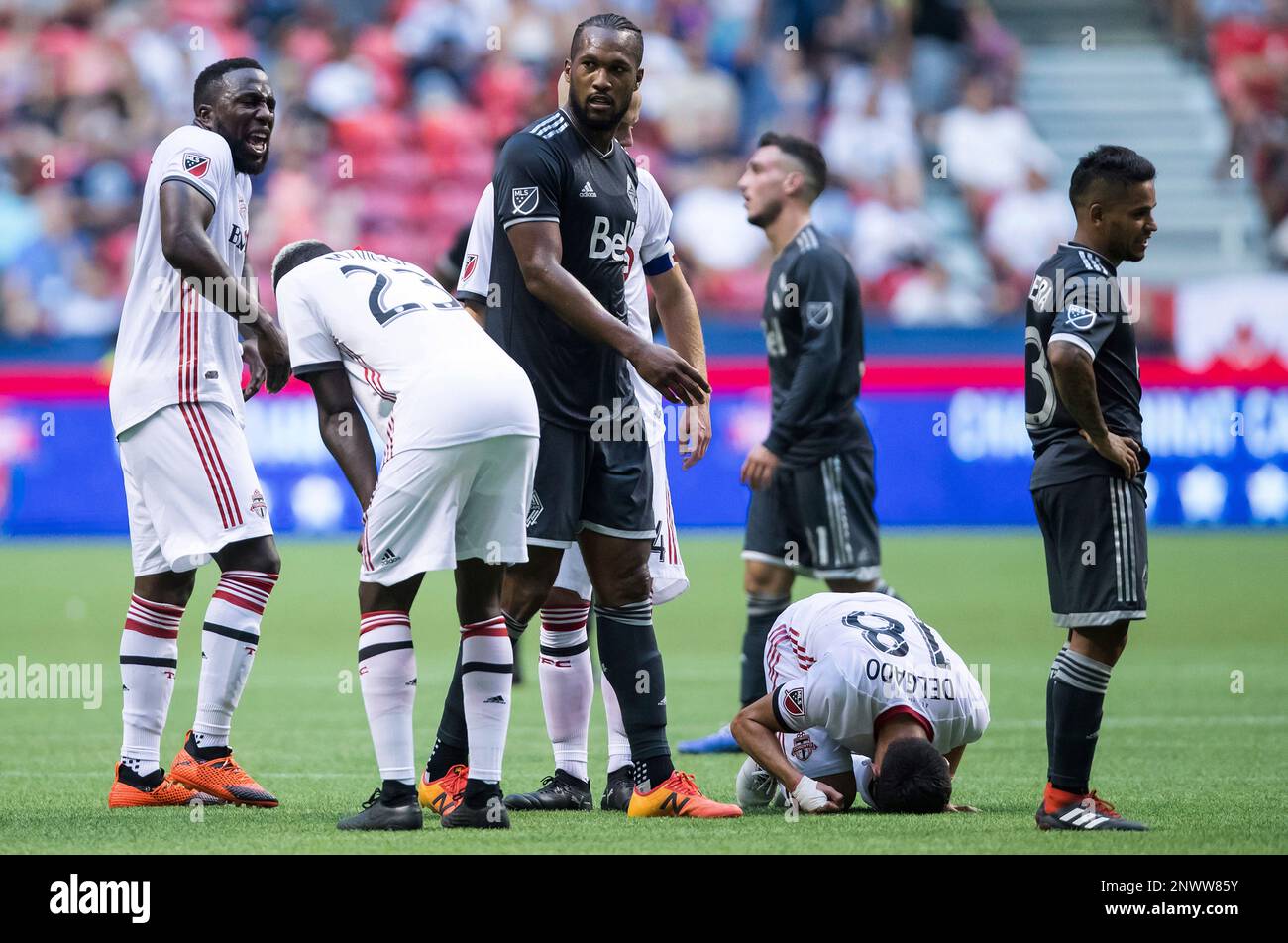 Toronto FC's Marky Delgado (18) kneels on the ground after being tackled by Vancouver Whitecaps' Felipe Martins, not seen, as Kendall Waston, center, and Cristian Techera, right, stand nearby during the first half in the first leg of the Canadian soccer championship, Wednesday, Aug. 8, 2018, in Vancouver, British Columbia. (Darryl Dyck/The Canadian Press via AP) Banque D'Images