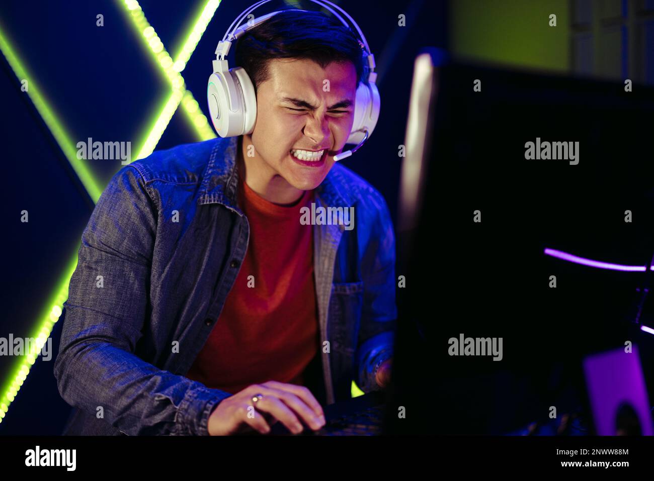 Le gamer se moque de la frustration en se faisant passer d'une balle dans un moment intense de jeu sur pc. Jeune homme portant un casque et jouant à un jeu vidéo sur un Banque D'Images