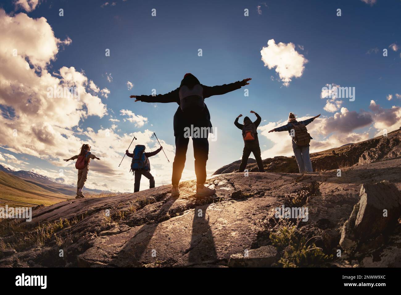 Groupe de randonneurs silhouettes se dresse dans le vainqueur pose avec les bras ouverts contre le soleil et les montagnes de coucher de soleil Banque D'Images