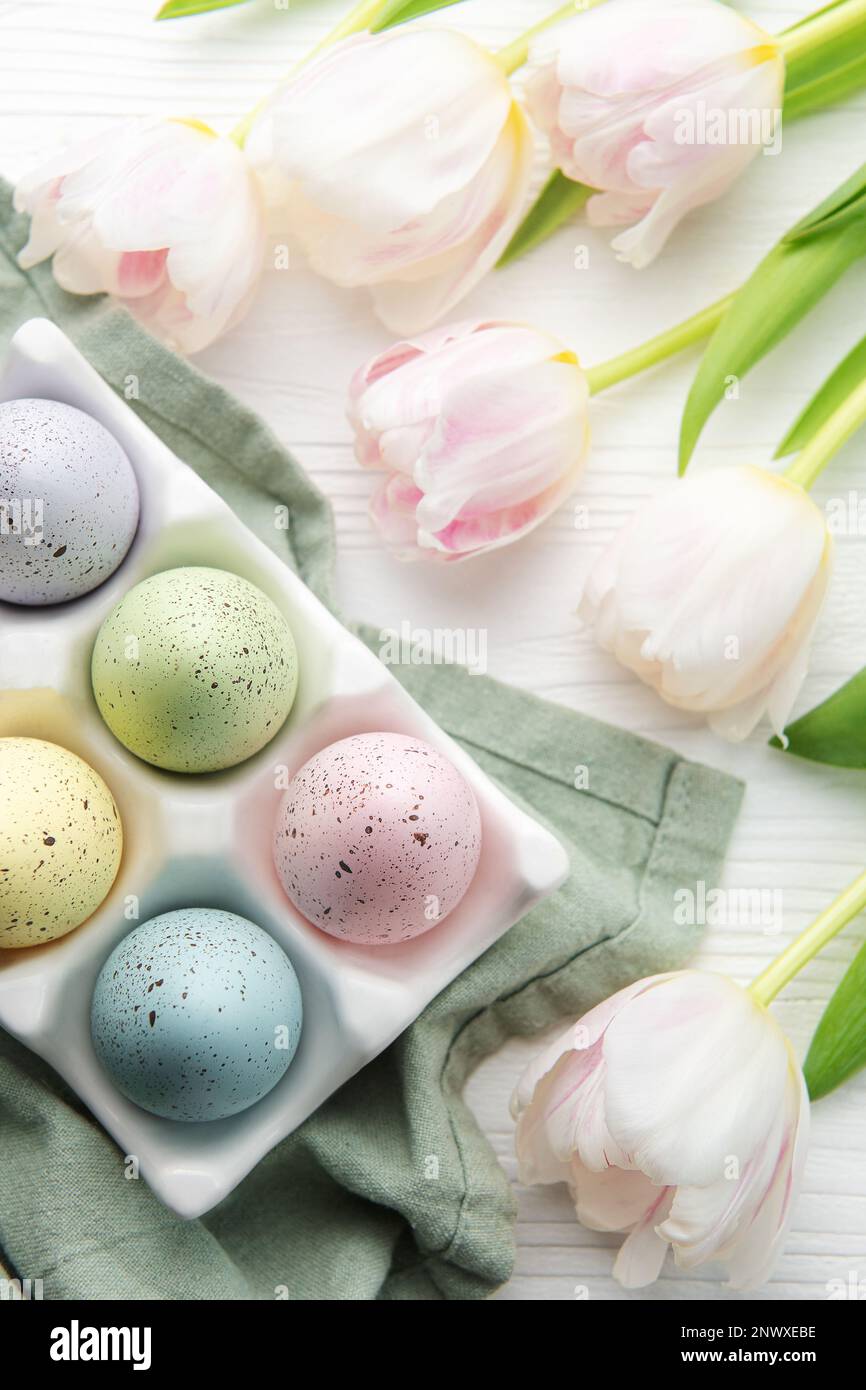 Porte-oeufs de Pâques peint couleurs pastel et tulipes roses sur fond blanc en bois. Vue de dessus. Espace pour le texte. Banque D'Images