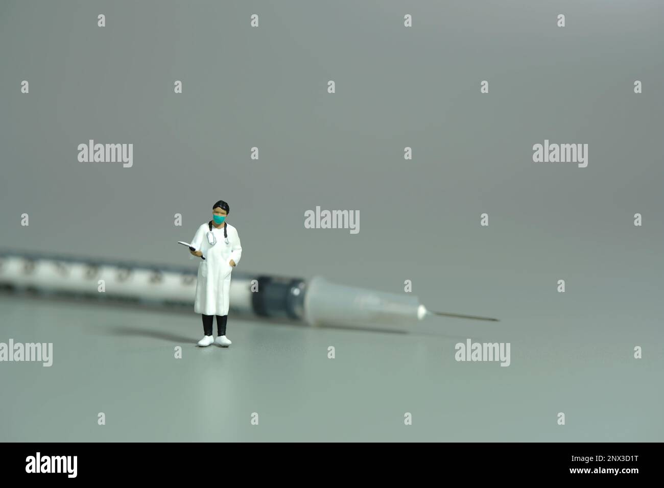 Photographie miniature de personnage de jouet de personnes. Une femme médecin debout devant la seringue à aiguille sur fond gris. Photo d'image Banque D'Images