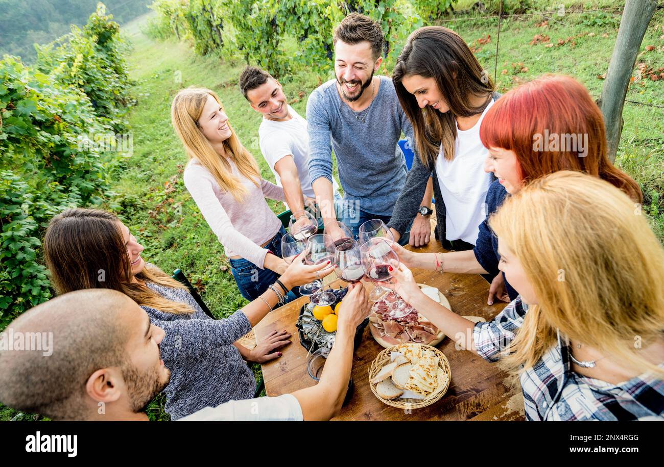 Jeunes amis ayant plaisir à l'extérieur clinking verres à vin rouge - heureux gens mangeant du raisin et de boire au moment de la récolte dans la ferme vignoble cave - vous Banque D'Images