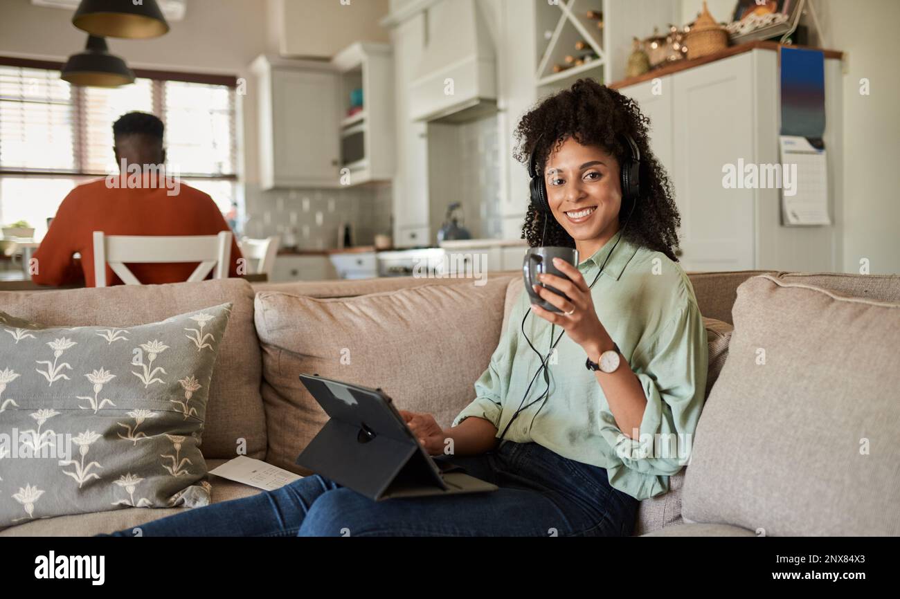 Femme souriante portant un casque et utilisant une tablette sur son canapé Banque D'Images