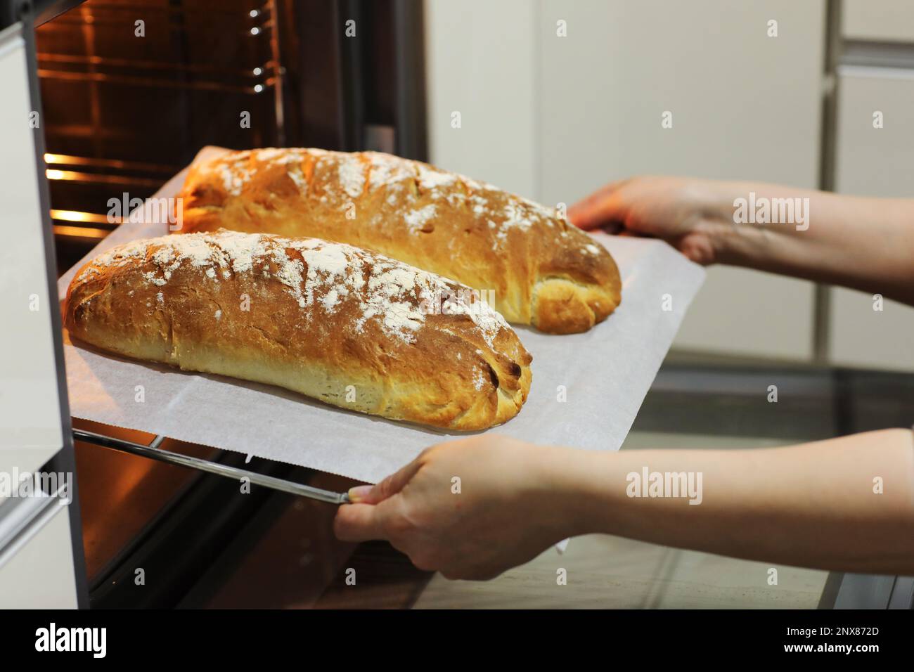 Photo de femmes les mains de prendre des pains chauds frais cuits d'un four électrique sur un plateau métallique dans la cuisine à la maison. Pain rustique fait maison, baki Banque D'Images