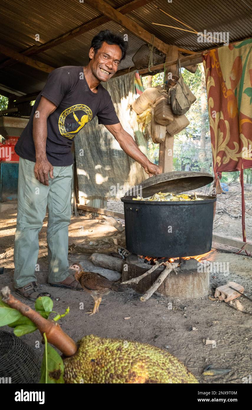 Un homme dans un village cambodgien rural sourit alors qu'il vérifie le pot de cuisine de porc composé de jackfruit et de tronc de bananiers. Province de Siem Reap, Banque D'Images