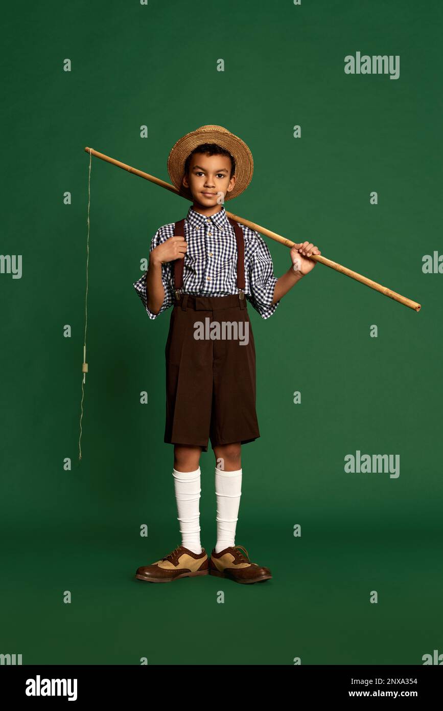 Joli petit garçon, enfant en chemise à carreaux et short suspendu isolé sur fond vert foncé. Concept d'enfance, amitié, rétro Banque D'Images