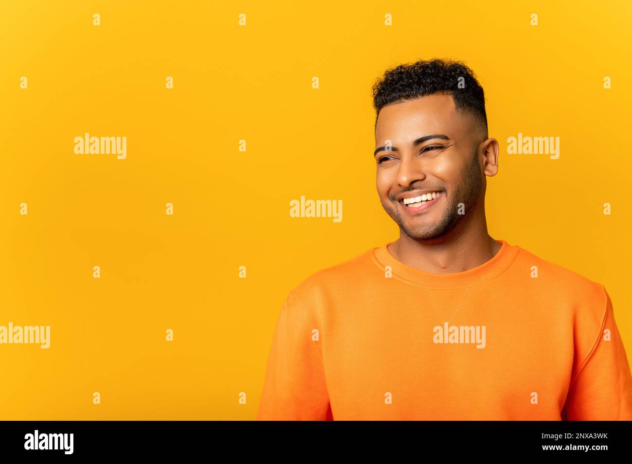 Portrait d'un jeune Indien heureux et satisfait, debout avec le sourire et regardant loin. Studio d'intérieur tourné sur fond jaune Banque D'Images