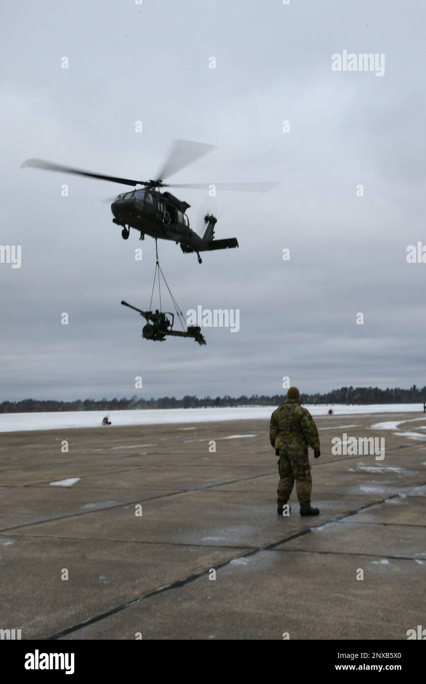 Un UH-60 Blackhawk du 1-147th Aviation Regiment, de la Garde nationale du Michigan, lève un obusier de M119 du 1-120th Field Artillery Regiment, de la Garde nationale du Wisconsin, tout en effectuant une charge de harnais pendant la grève du Nord 23-1, le 23 janvier 2023, à l'aérodrome de l'Armée de Grayling, au Michigan. La répétition hivernale de la grève du Nord constitue un moyen rentable pour les unités du ministère de la Défense de mener des opérations conjointes, par temps froid, dans tous les domaines. Banque D'Images