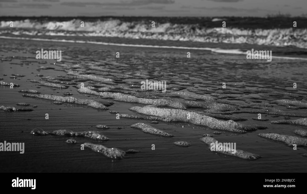 Vagues et motifs de vagues sur une plage de Walton sur la Naze dans l'Essex. Une journée venteuse. Mousse sur sable. Banque D'Images