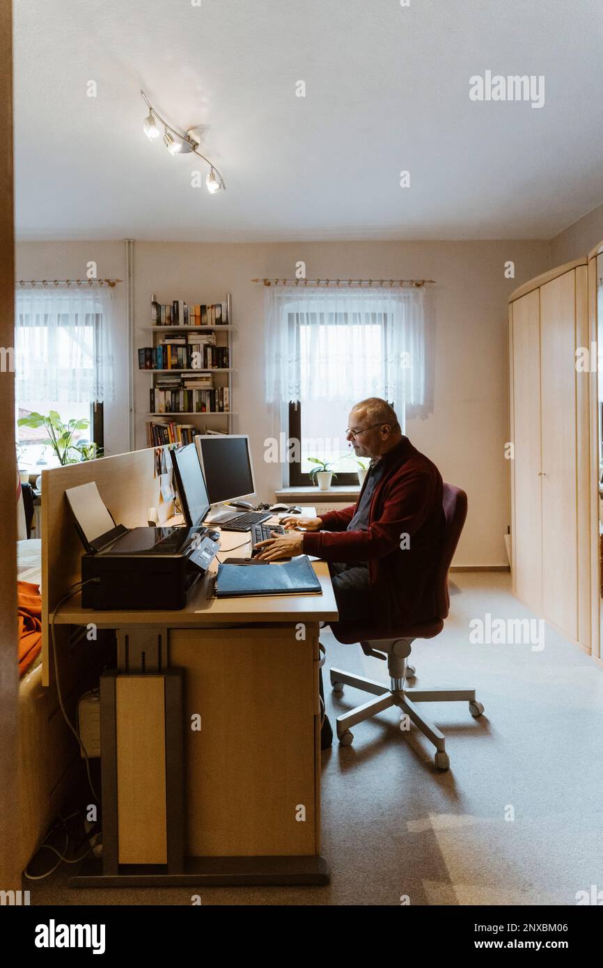Vue latérale de l'homme âgé utilisant un ordinateur au bureau à la maison Banque D'Images