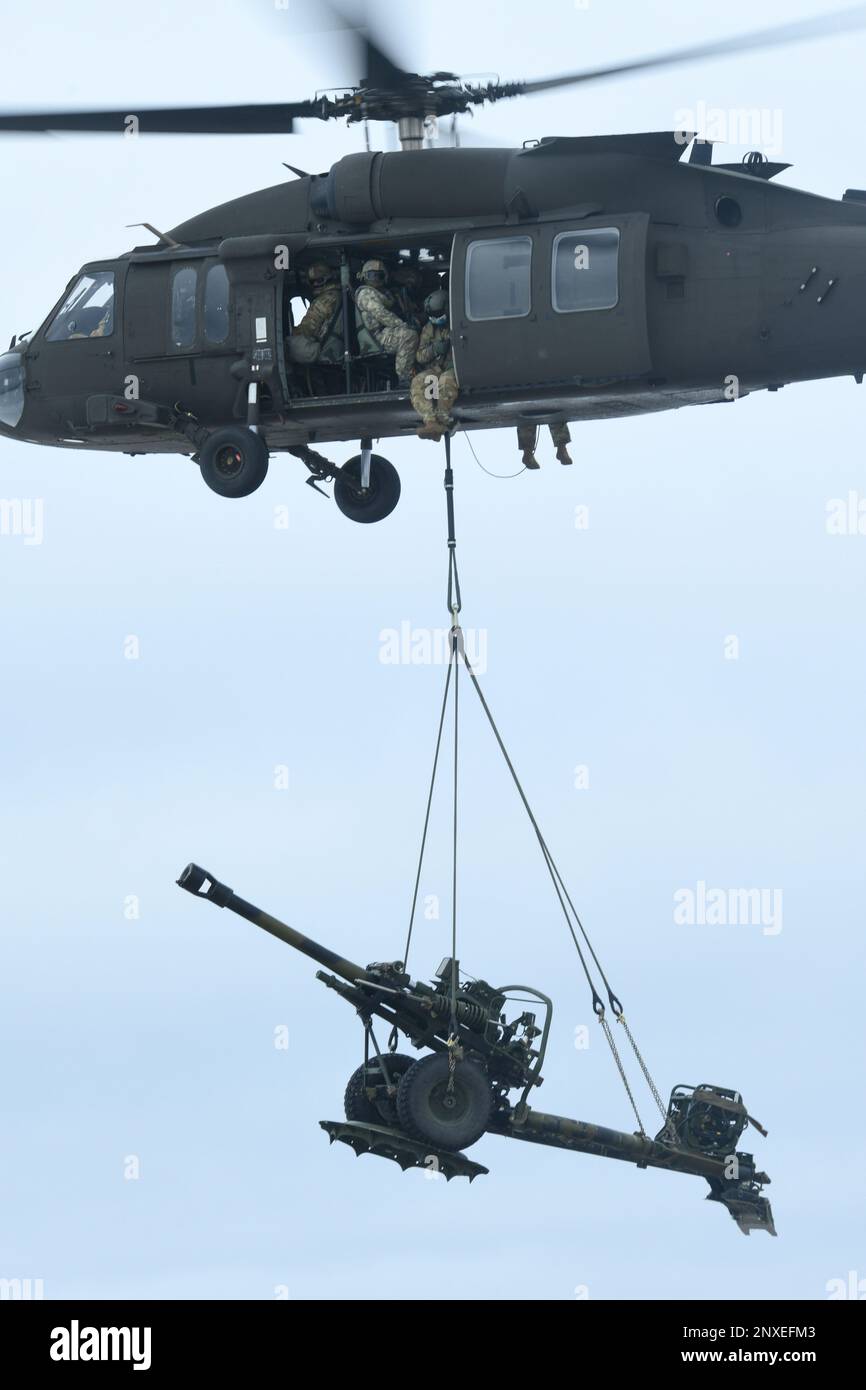 Un UH-60 Blackhawk du 1-147th Aviation Regiment, de la Garde nationale du Michigan, lève un obusier de M119 du 1-120th Field Artillery Regiment, de la Garde nationale du Wisconsin, tout en effectuant une charge de harnais pendant la grève du Nord 23-1, le 23 janvier 2023, à l'aérodrome de l'Armée de Grayling, au Michigan. La répétition hivernale de la grève du Nord constitue un moyen rentable pour les unités du ministère de la Défense de mener des opérations conjointes, par temps froid, dans tous les domaines. Banque D'Images