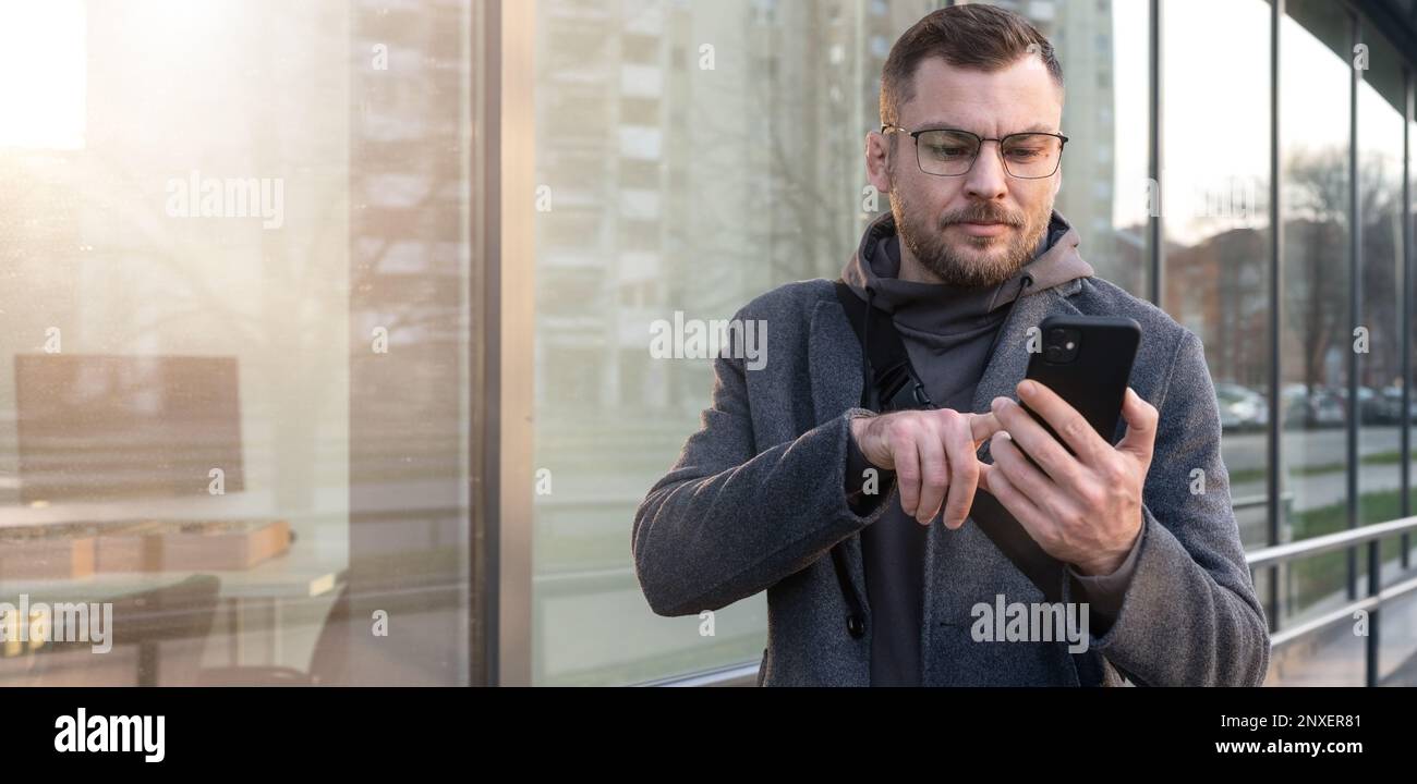 Homme entrepreneur portant des lunettes en utilisant son smartphone à l'extérieur dans la ville, homme lisant le massage d'email sur le téléphone mobile. Banque D'Images