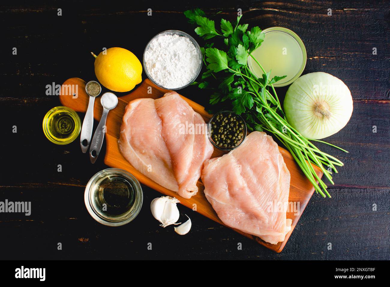 Ingrédients sains de picata de poulet sur une table en bois : Eclaircir les ingrédients de picata de poulet sur un fond sombre Banque D'Images
