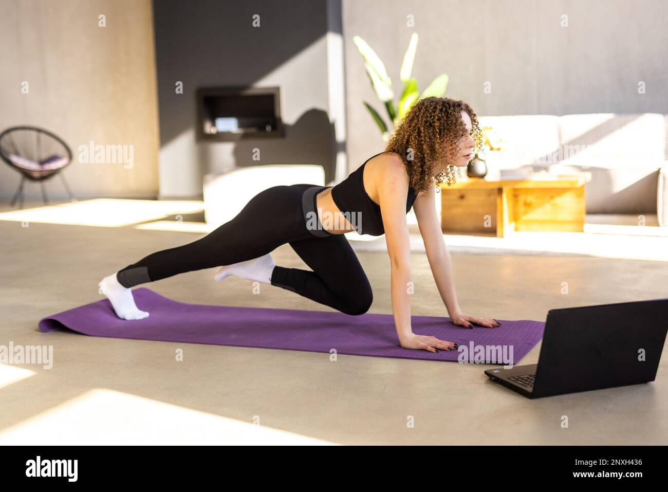 Femme souriante s'exerçant à la maison et regardant des vidéos de formation sur un ordinateur portable. Femme faisant des planches avec une jambe tendue et regardant un ordinateur portable. Banque D'Images