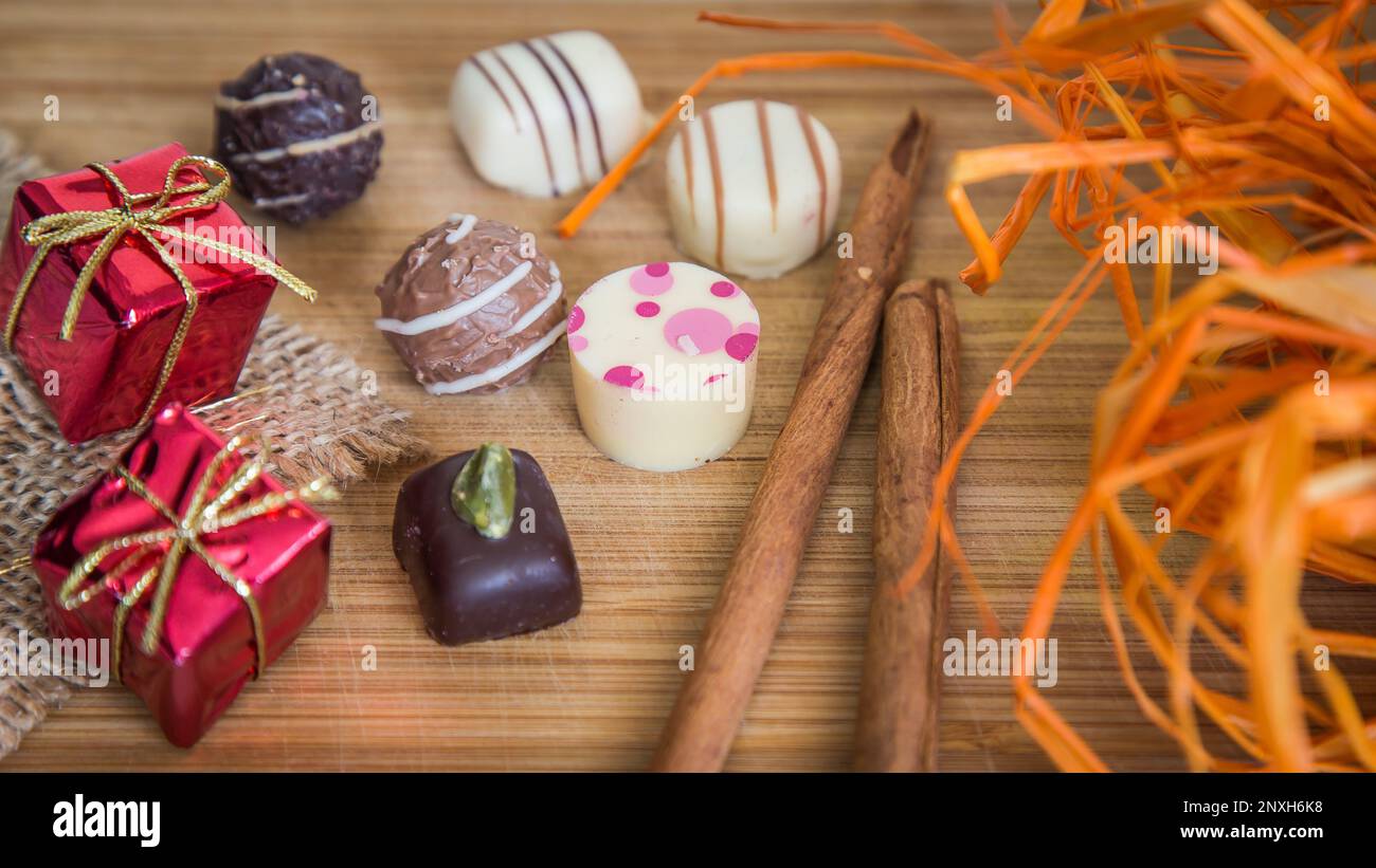 Pralines au chocolat avec points roses. Petits paquets rouges et décoration orange, avec bâton de cannelle. Banque D'Images