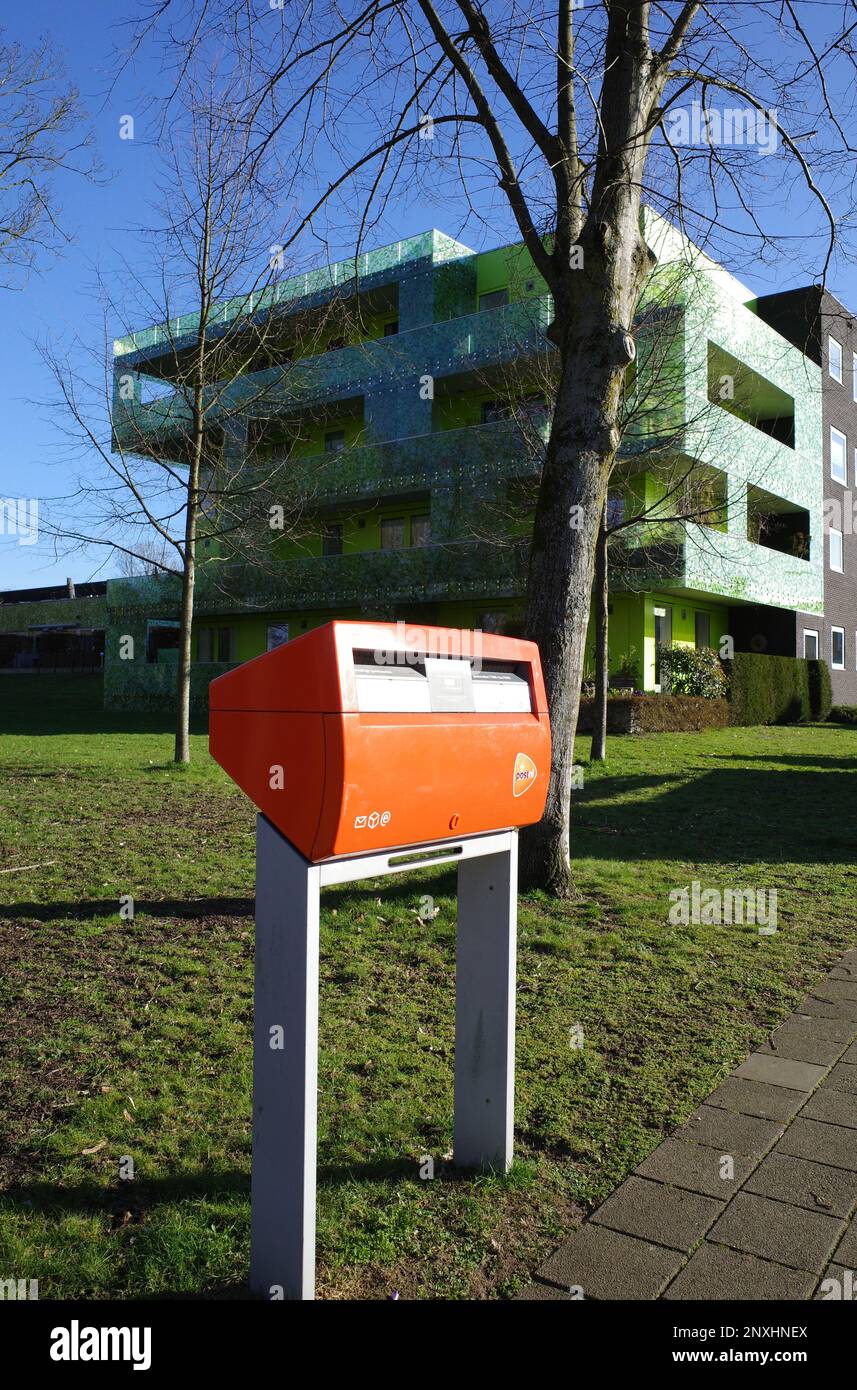 Beekbergen, pays-Bas - Fév 28 2023 une boîte aux lettres orange devant un immeuble moderne et vert situé au coeur du village de Beekbergen. Banque D'Images
