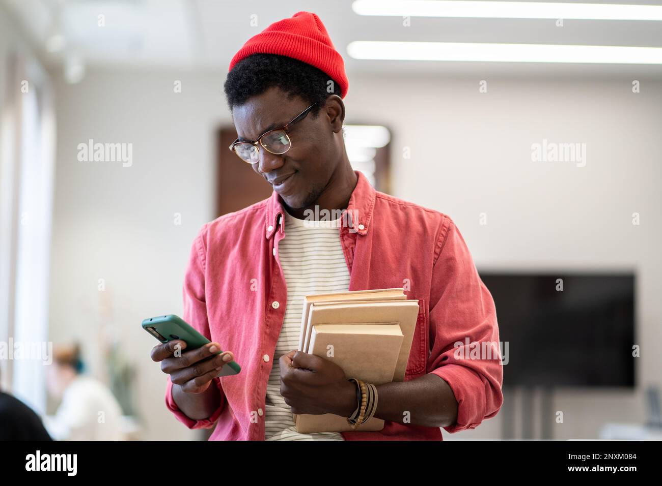 Homme afro-américain enseignant debout dans la bibliothèque à l'aide de l'application de planification sur un appareil mobile Banque D'Images