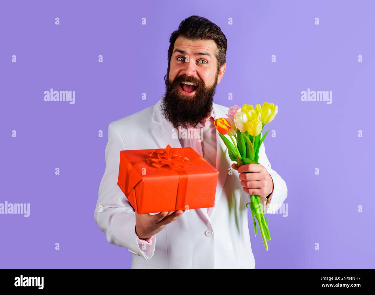 Homme barbu souriant avec boîte cadeau et bouquet de fleurs. Homme d'affaires en costume avec cadeau et bouquet de tulipes. Homme romantique avec bouquet de fleurs Banque D'Images