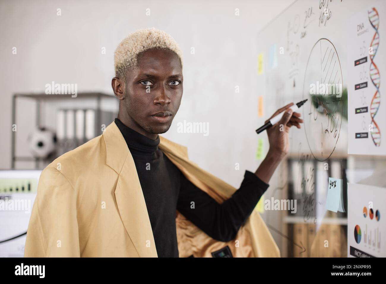 Jeune Africain confiant en tenue formelle écrivant à bord avec des autocollants en papier lors d'une réunion d'affaires dans une salle de bureau. Conférence de travail et concept de personnes. Banque D'Images