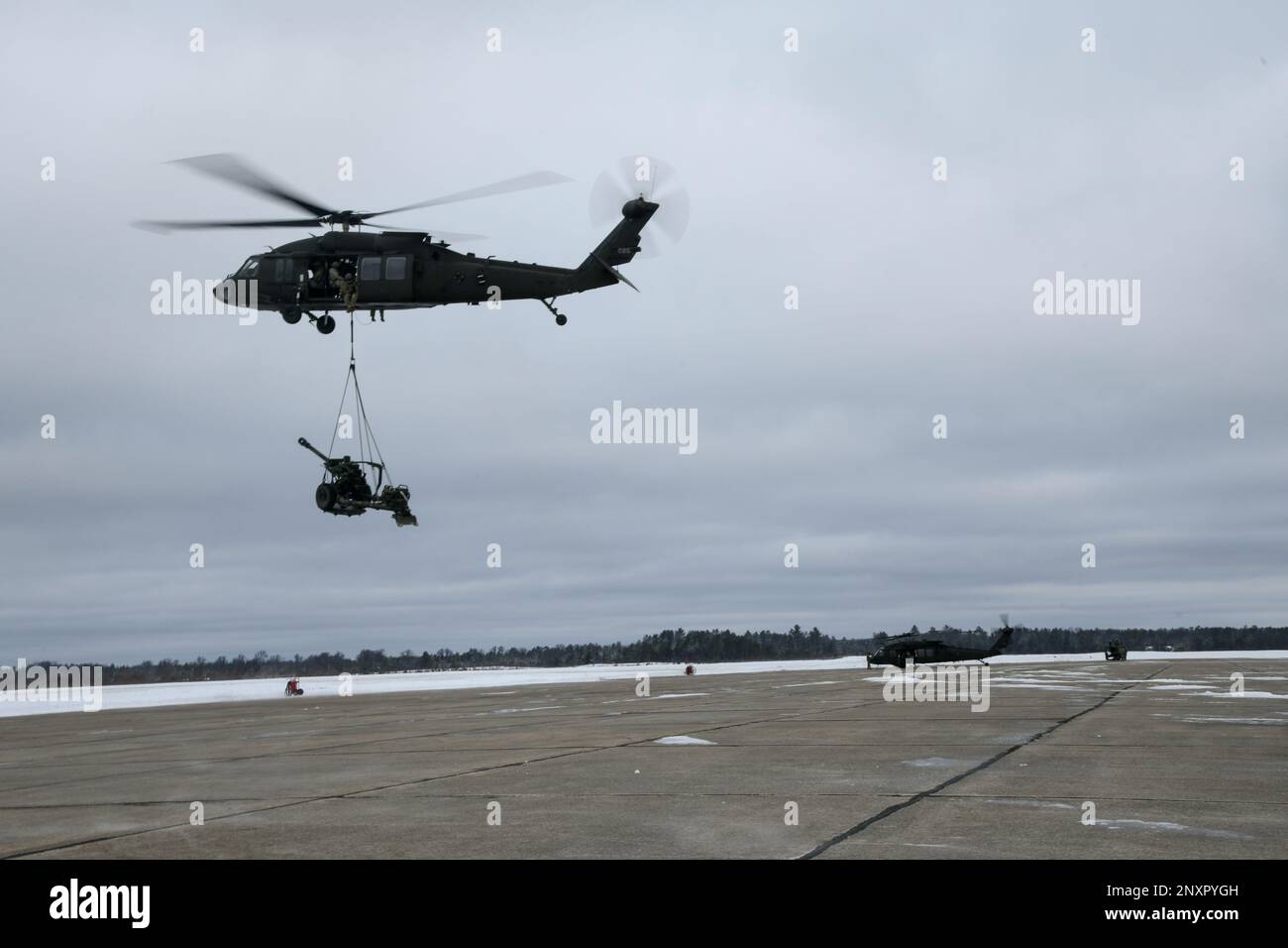 Un UH-60 Blackhawk du 1-147th Aviation Regiment, de la Garde nationale du Michigan, lève un obusier de M119 du 1-120th Field Artillery Regiment, de la Garde nationale du Wisconsin, tout en effectuant une charge de harnais pendant la grève du Nord 23-1, le 23 janvier 2023, à l'aérodrome de l'Armée de Grayling, au Michigan. La répétition hivernale de la grève du Nord constitue un moyen rentable pour les unités du ministère de la Défense de mener des opérations conjointes, par temps froid, dans tous les domaines. Banque D'Images