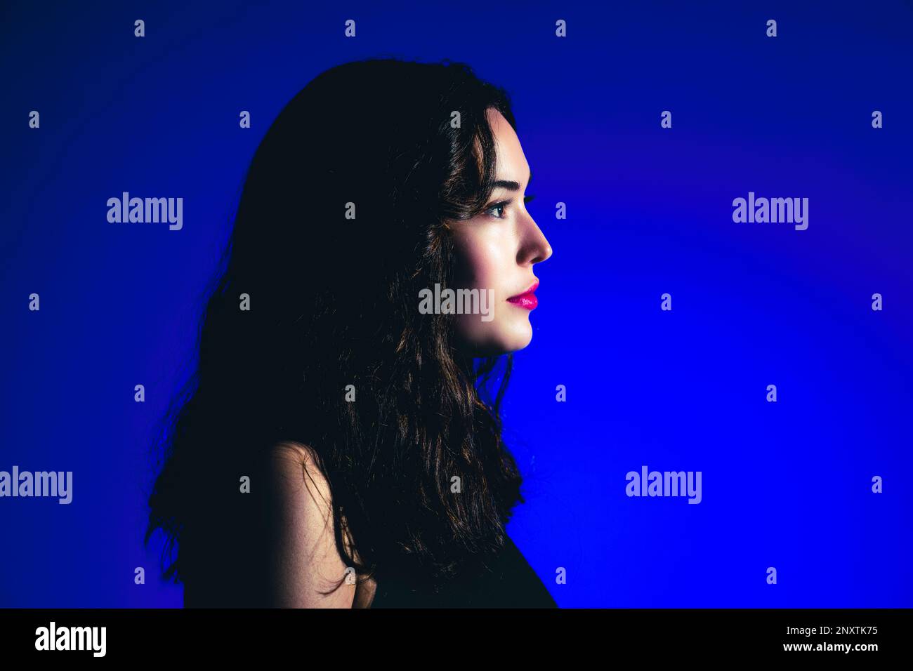 Gros plan sur le côté de la jeune femme dans le profil sur fond bleu | couleurs vives Banque D'Images
