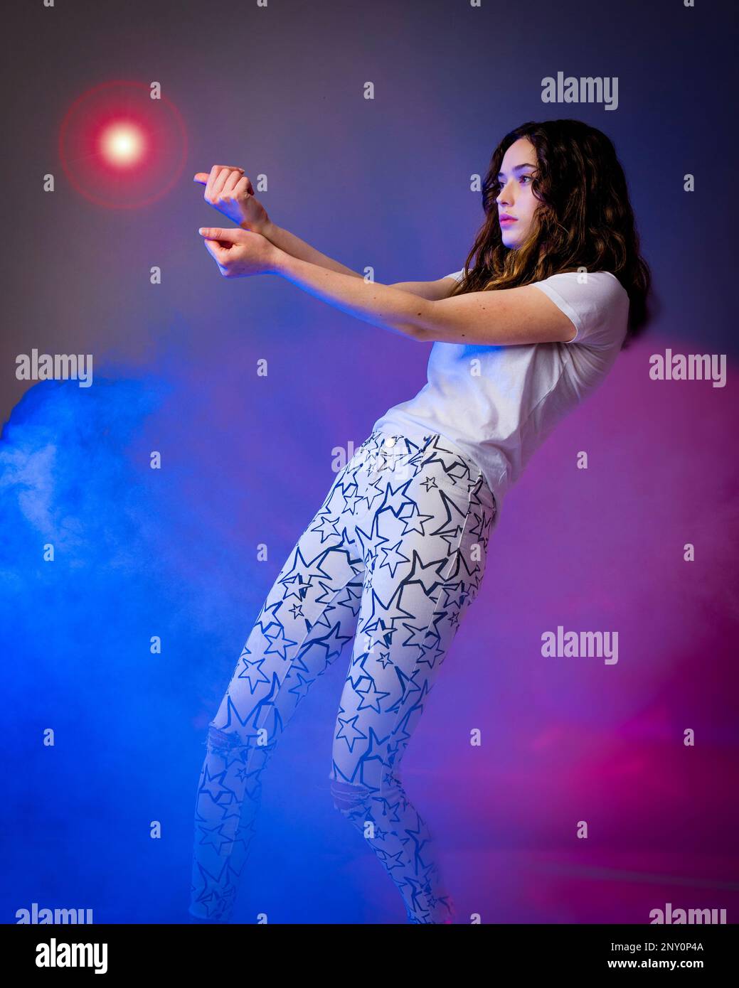 Adolescente debout dans un brouillard bleu et rouge exécutant la magie avec le bal de lumière | fantaisie Banque D'Images