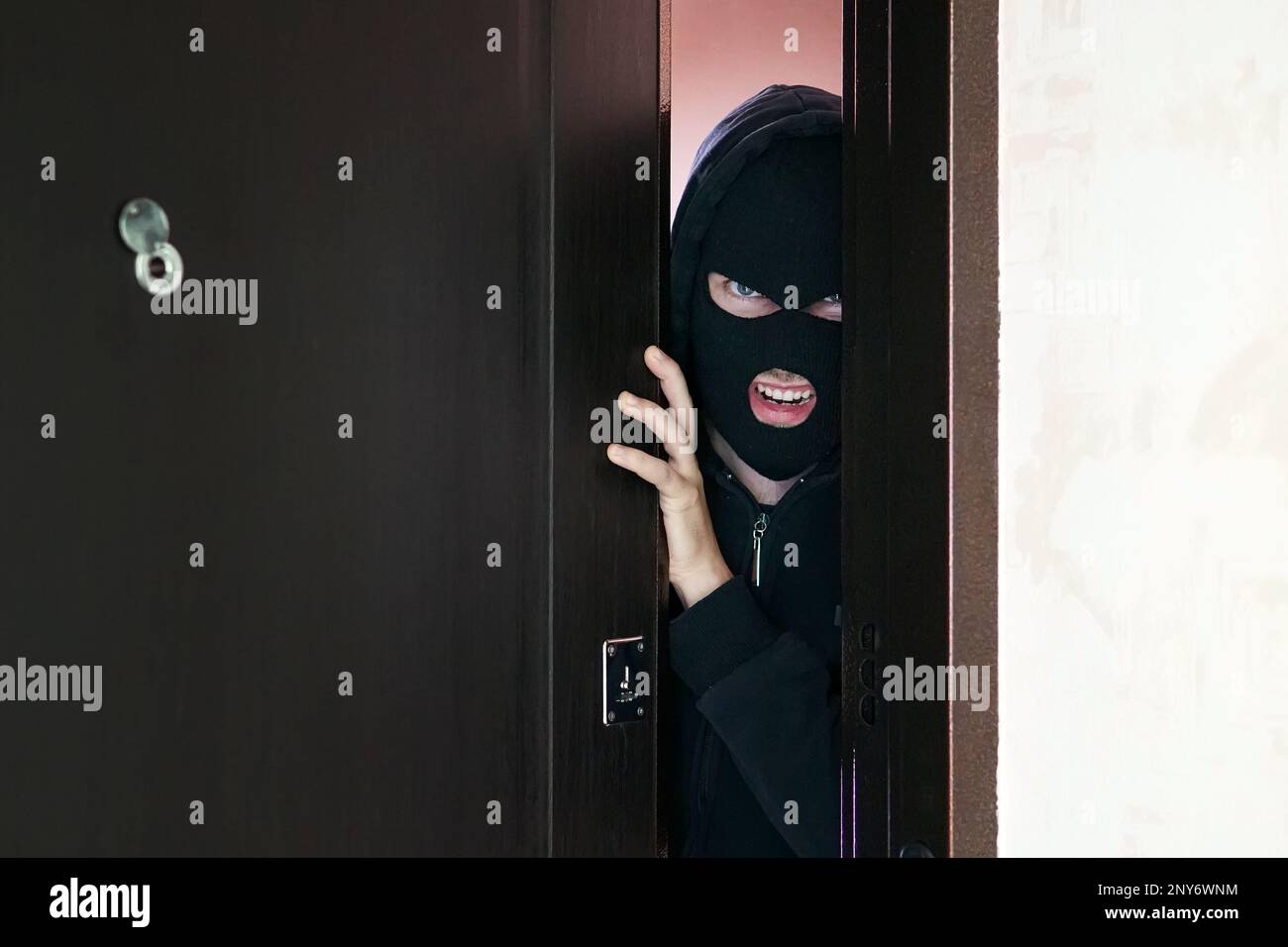 Un homme cambrioleur dans le masque noir ouvrir la porte voler quelque chose de la maison. le