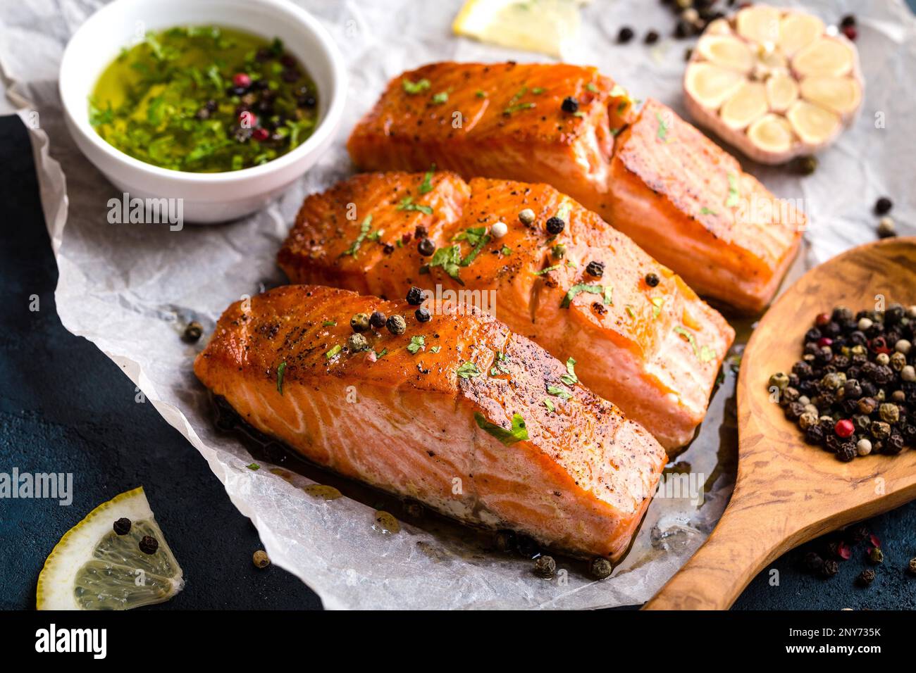 Délicieux filet de saumon frit, assaisonnements sur table en béton rustique bleu. Steak de saumon cuit au poivre, aux herbes, au citron, à l'ail, à l'huile d'olive, à la cuillère. Banque D'Images