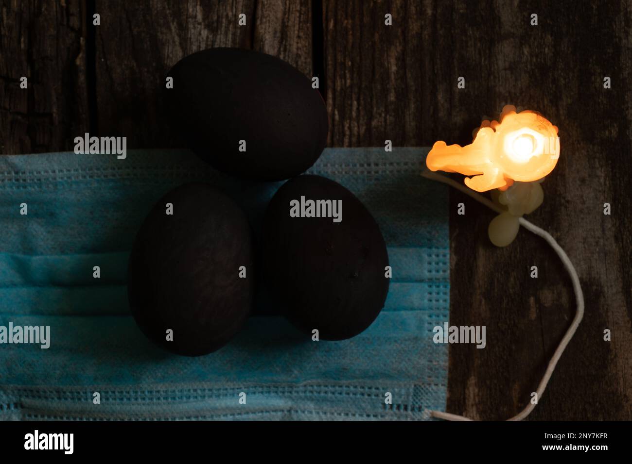 Masque médical et bougies aux œufs noirs le jour de Pâques sur une vieille table en bois pendant la pandémie Banque D'Images