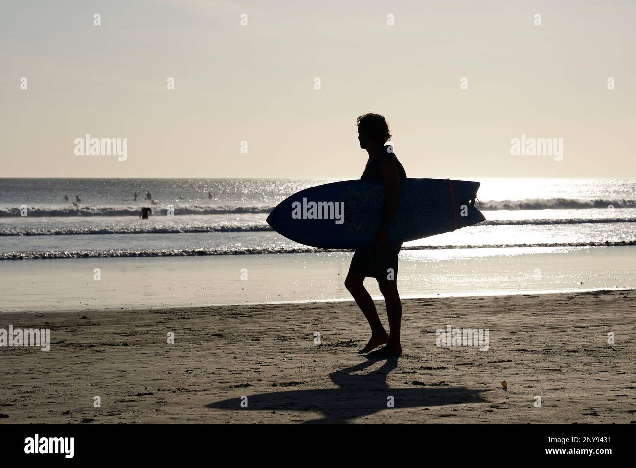 Silhouette d'un jeune homme qui marche le long d'une plage de sable avec une planche de surf nichée sous son bras, le Nicaragua Banque D'Images