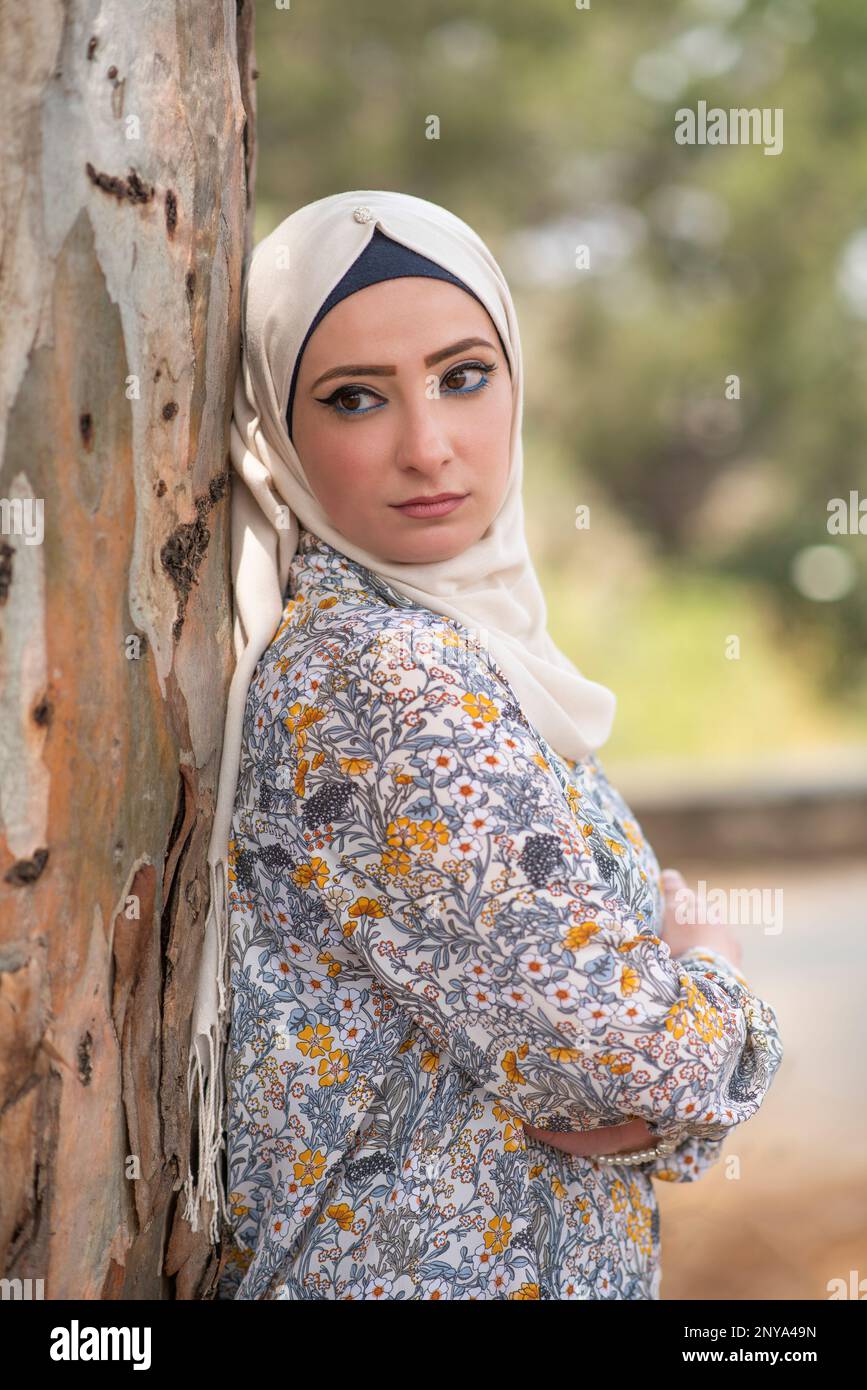 Belle femme musulmane portant le hijab penchée contre l'arbre en regardant loin Banque D'Images