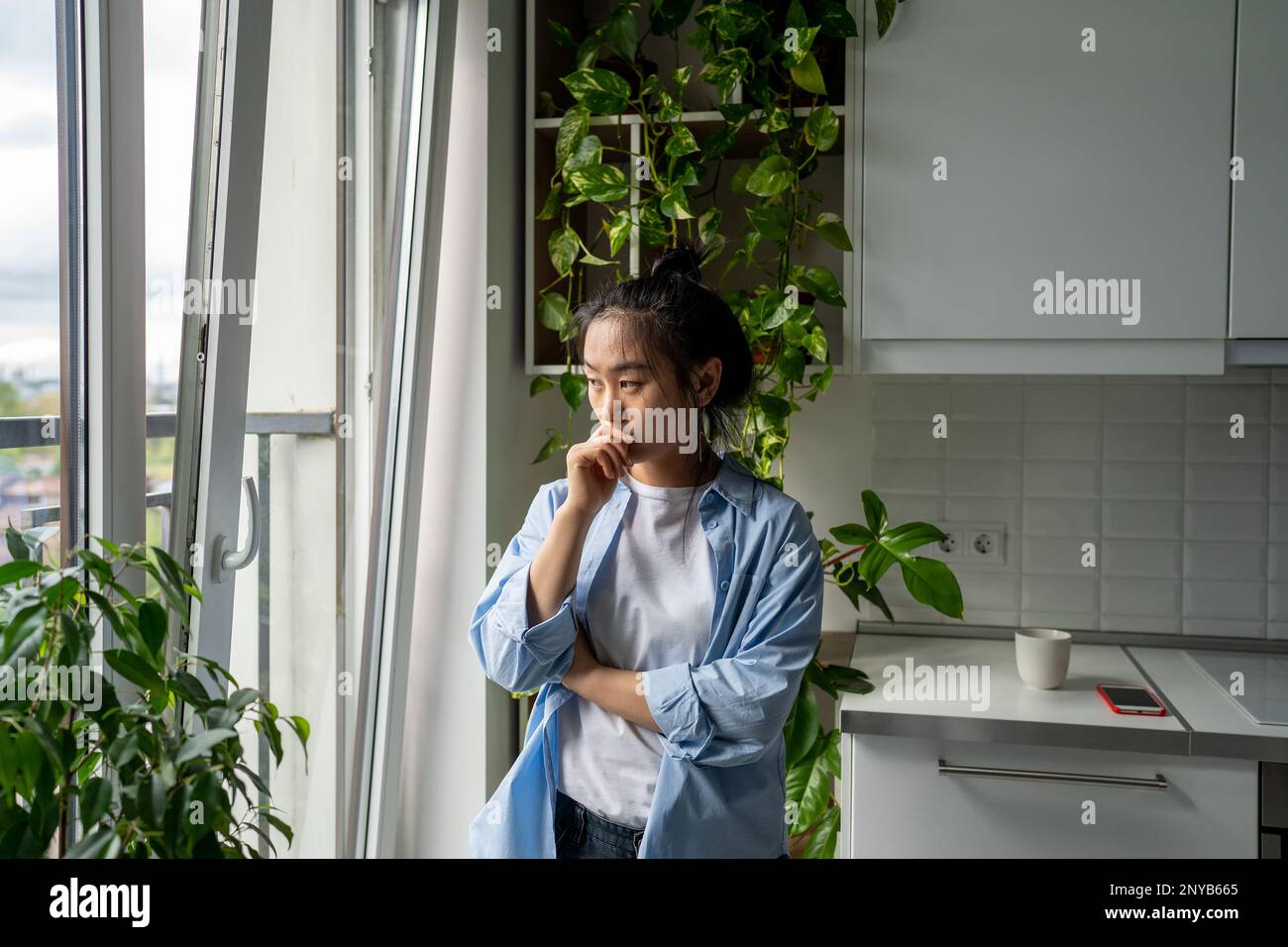 Femme pensive debout à la maison regardant la fenêtre réfléchir avant de prendre la décision Banque D'Images