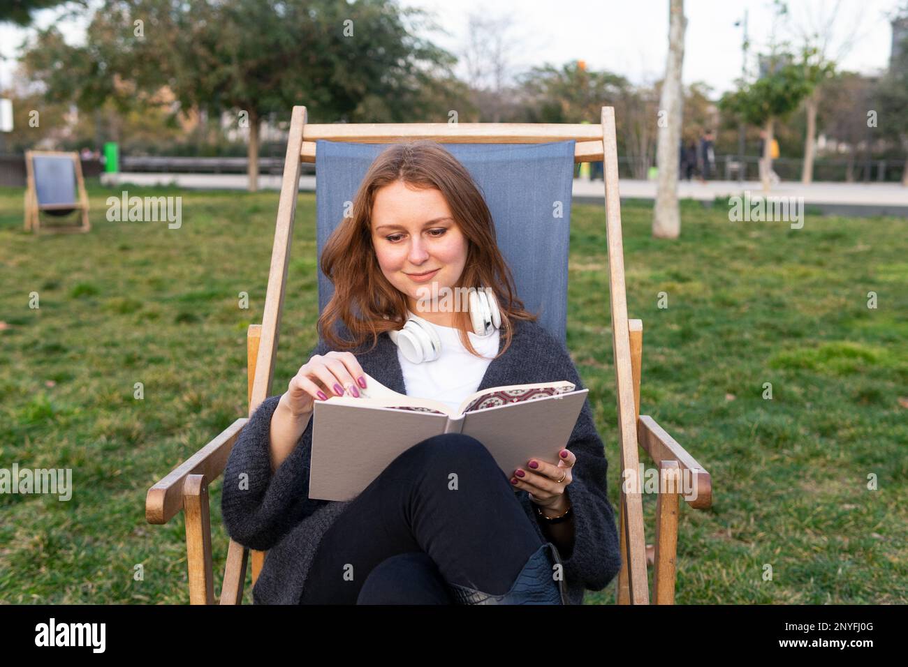 Bonne femme portant un pull chaud avec écouteurs lisant l'histoire de  fiction et souriant tout en se relaxant dans une chaise longue dans le parc  Photo Stock - Alamy