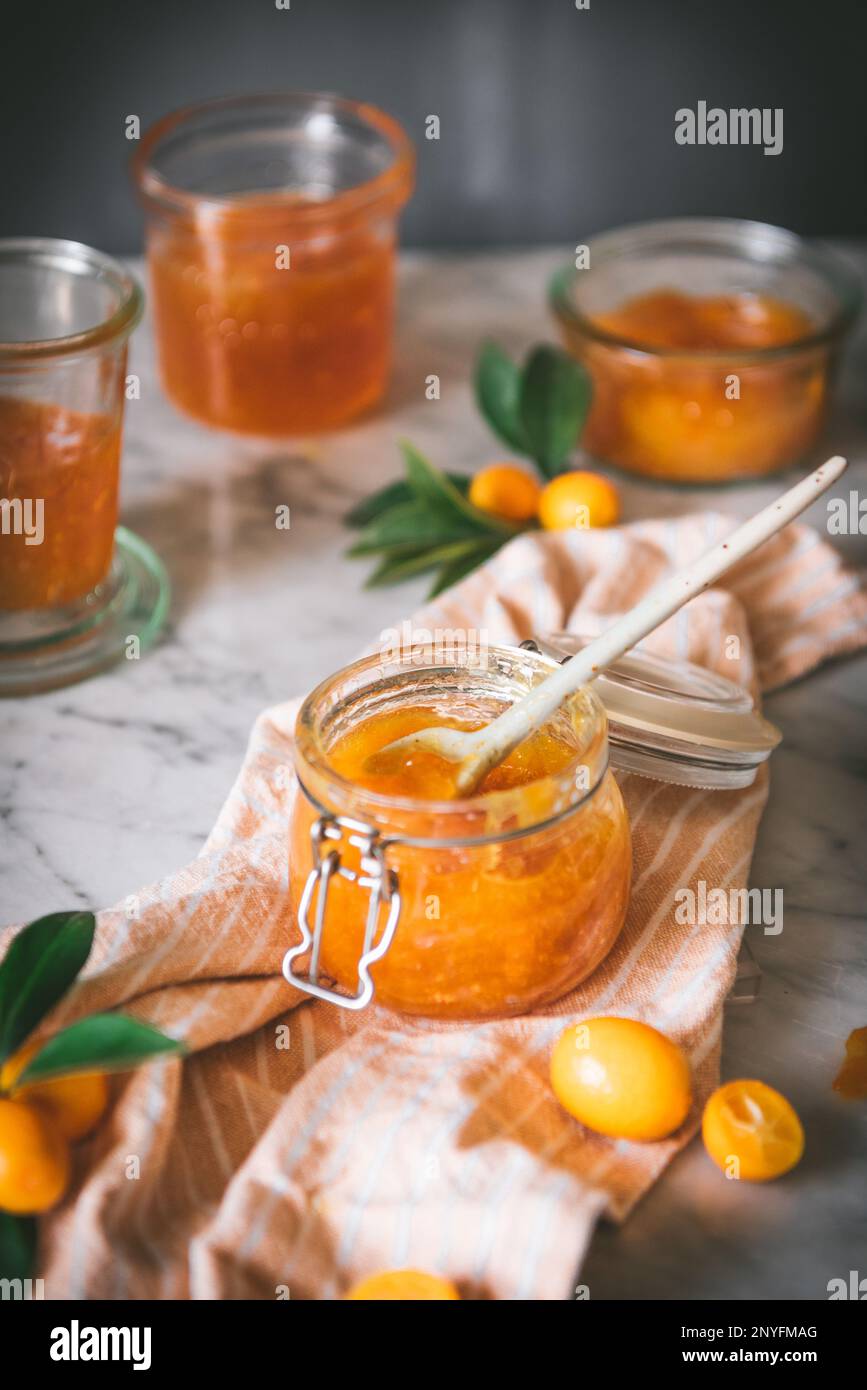 Gros plan du bol en verre avec confiture de kumquat fraîche avec une cuillère sur une table sur fond gris foncé flou Banque D'Images
