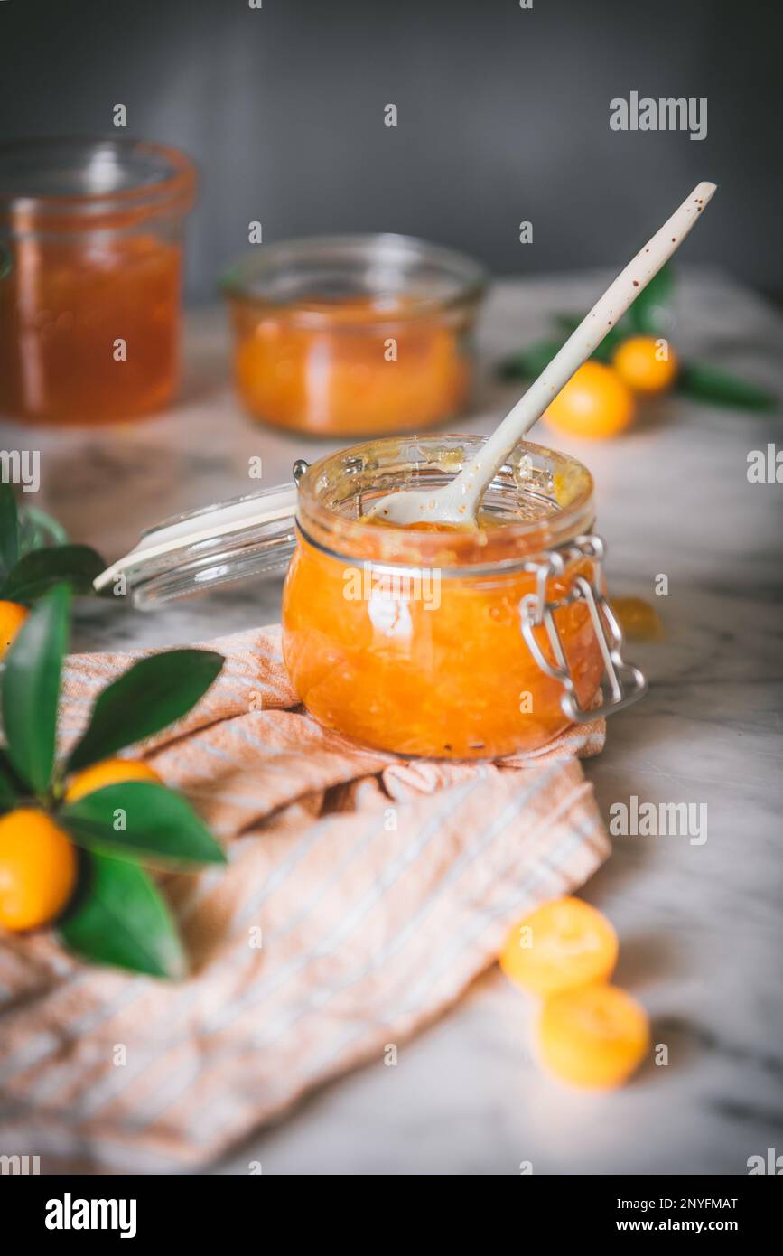 Gros plan du bol en verre avec confiture de kumquat fraîche avec une cuillère sur une table sur fond gris foncé flou Banque D'Images