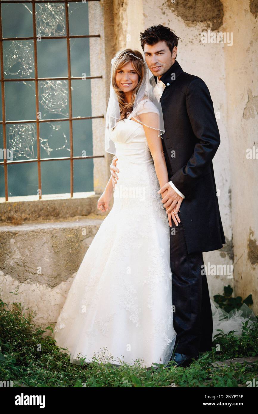Homme attrayant en costume élégant et jolie femme en blanc habillez-vous en souriant et regardez l'appareil photo tout en vous tenant près du vieux bâtiment Banque D'Images