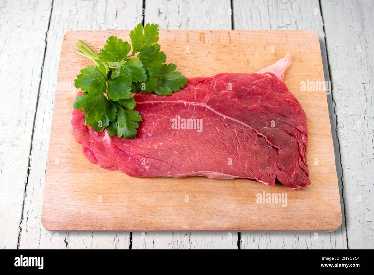 Steak de bœuf cru sur une planche à découper en bois avec des feuilles de persil isolées sur un chemin d'écrêtage blanc Banque D'Images