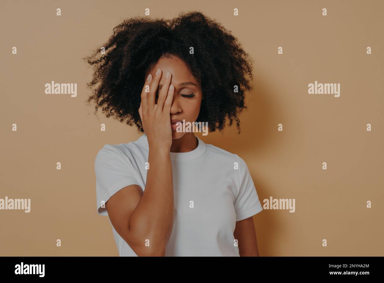 Photo studio de jeune femme bouleversée de race mixte frustrée par des problèmes dans la vie ou les relations, couvrant le visage avec la main et se sentant l'anxiété ou le déprr Banque D'Images