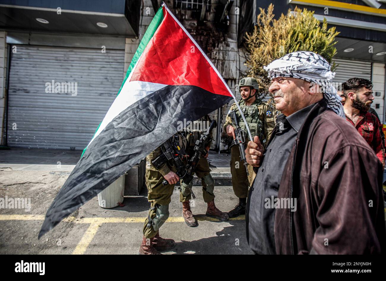 Naplouse, Palestine. 02nd mars 2023. Un homme palestinien âgé fait passer le drapeau palestinien devant les soldats israéliens lors d'une protestation contre les attaques des colons juifs et la fermeture des magasins commerciaux par l'armée israélienne dans la ville de Hawara, au sud de Naplouse, en Cisjordanie occupée. Crédit : SOPA Images Limited/Alamy Live News Banque D'Images