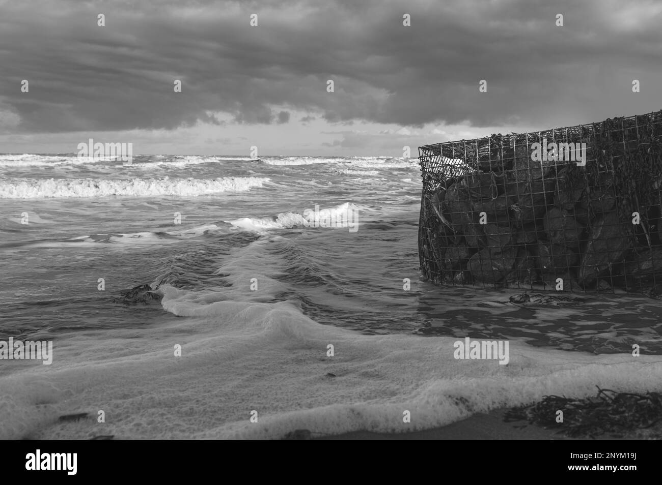 Panier de gabion avec des pierres sur une plage à Walton sur la Naze dans l'Essex. Froid, hiver, jour venteux. Les vagues s'écrasant contre le panier de gabion. Banque D'Images