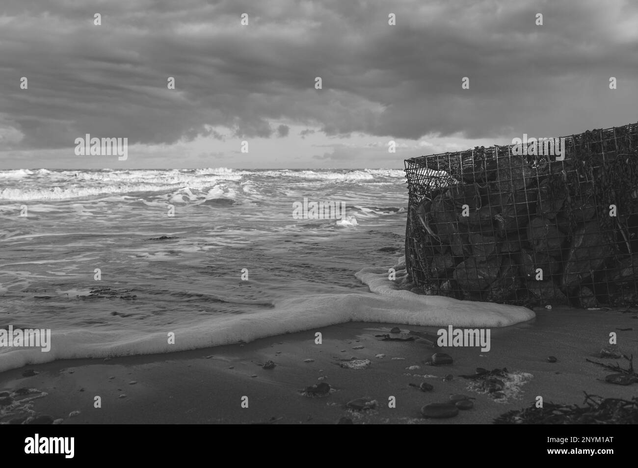 Panier de gabion avec des pierres sur une plage à Walton sur la Naze dans l'Essex. Froid, hiver, jour venteux. Les vagues s'écrasant contre le panier de gabion. Banque D'Images